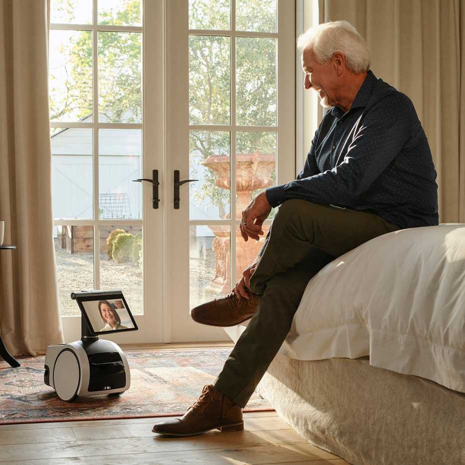 amazon astro robot is shown in the room with a man sitting on a bed interacting with it