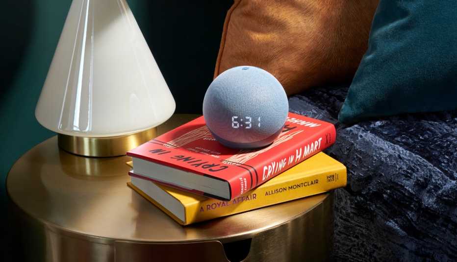 a smart speaker on top of some books on a night table by a bed