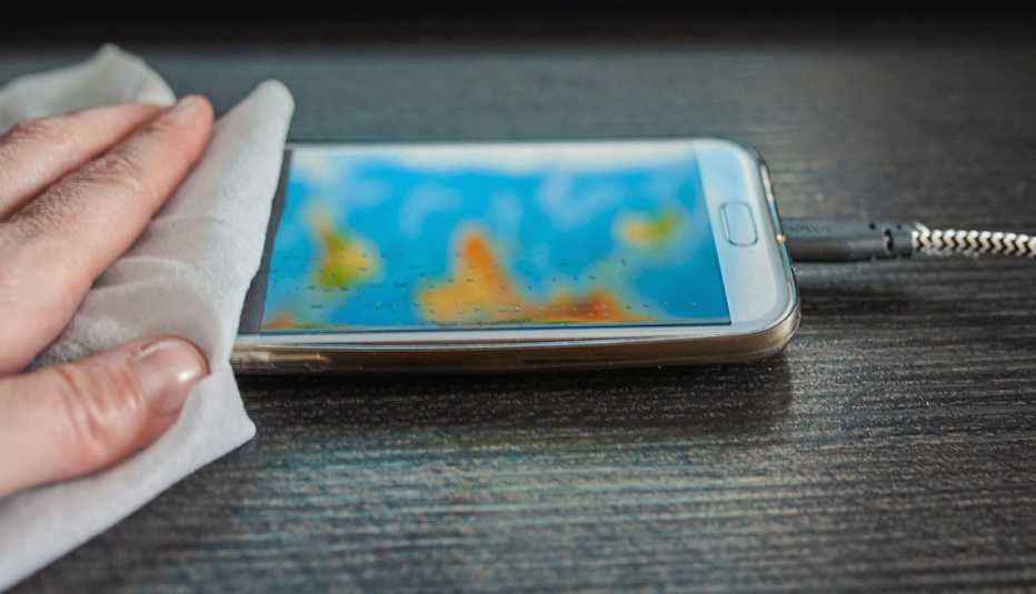 a person uses a cloth to clean the screen of a smartphone on a wooden surface