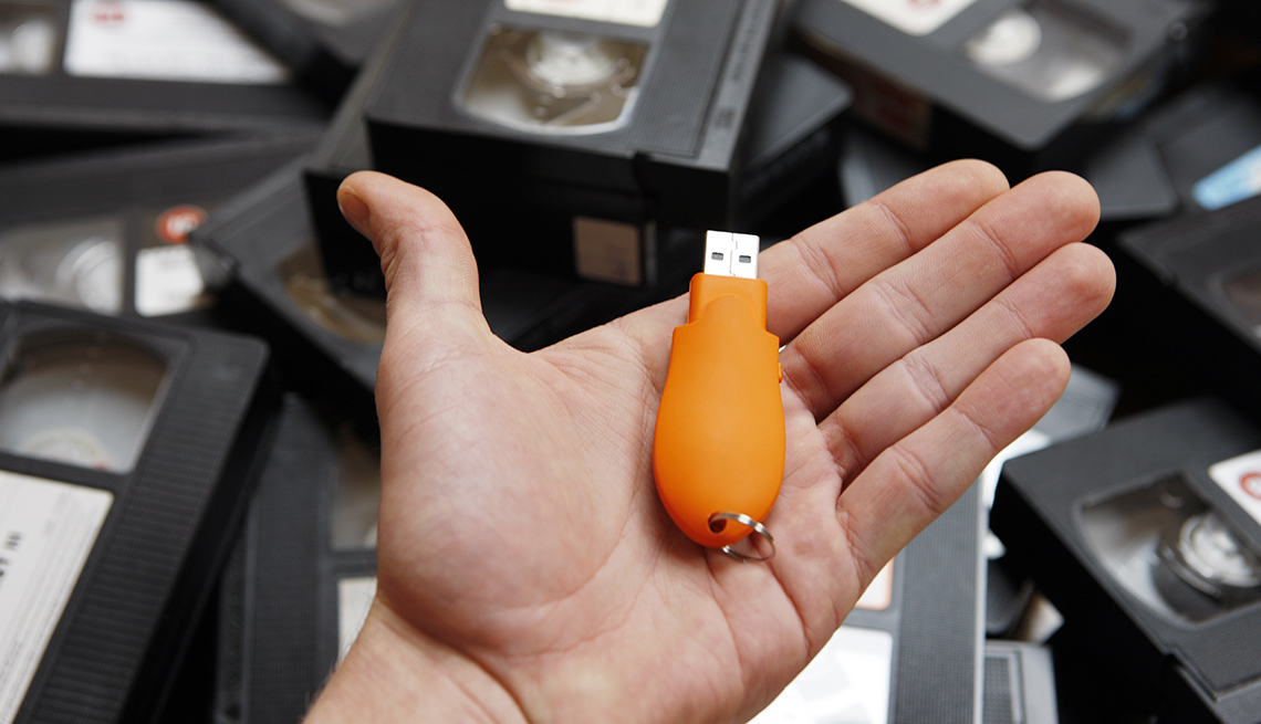 a memory stick in a man's hand over a pile of vhs tapes