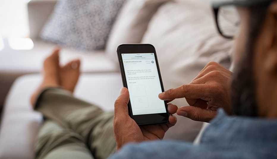 Closeup of a man hand holding cellphone with internet browser on screen. Man with spectacles relaxing sitting on couch while looking at mobile phone. Closeup of man using a smartphone to checking email at home.
