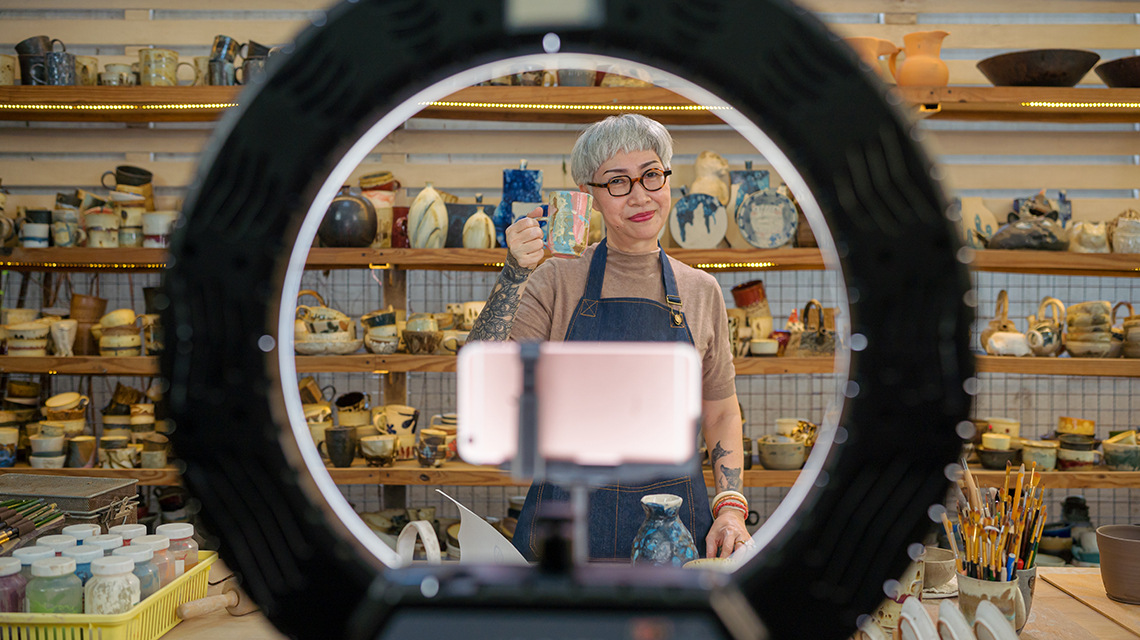 a woman is on camera with pottery and shelves in the background
