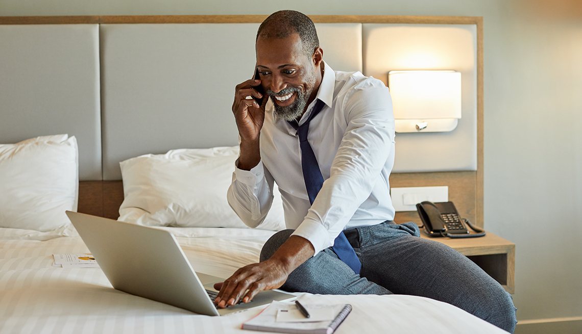 a man smiles as he talks on his smartphone while working in a hotel room