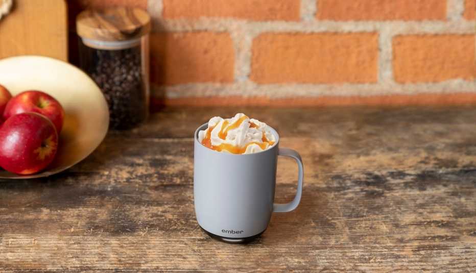 a horizontal picture of an ember mug full of whipped cream and caramel on a wooden surface