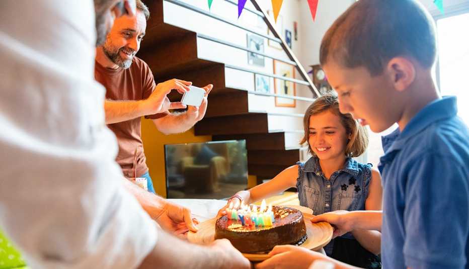 an older man with a beard takes a picture of two children with a chocolate birthday cake