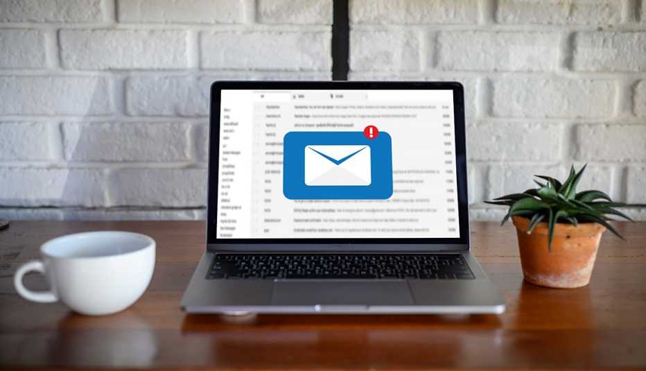 an image showing an icon for an unread email on a laptop sitting on a brown, wooden desk between a coffee cup and a plant