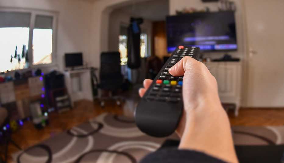a person extends their arm toward a television set while holding a remote control