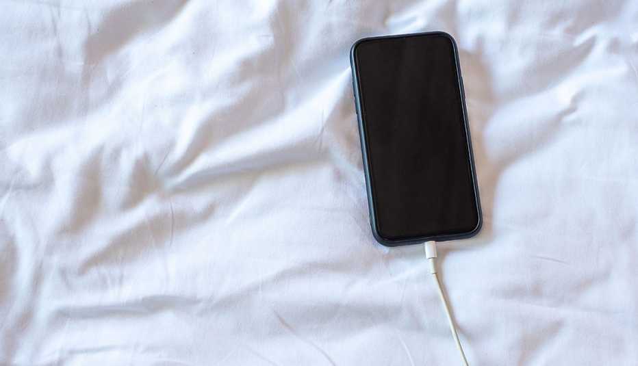 a black smartphone charging on a white bed