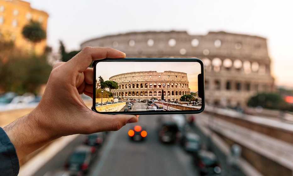 a person uses their phone to take a picture of the coliseum in rome