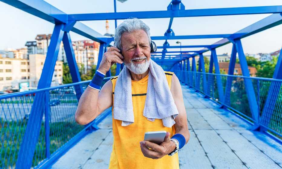 a man in a yellow t-shirt adjusts his headphones while holding a smartphone