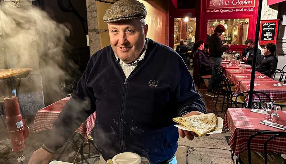 a smiling man in a cap holds out a crepe