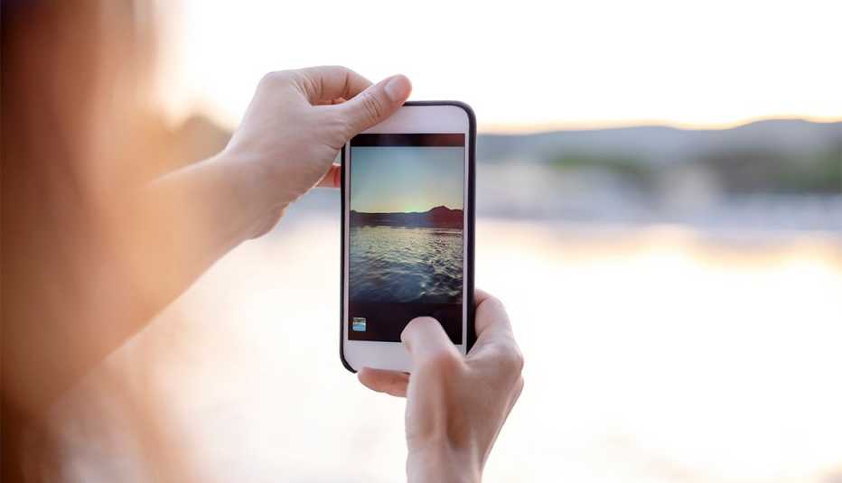 close up of a woman holding a smartphone taking a picture of a sunset