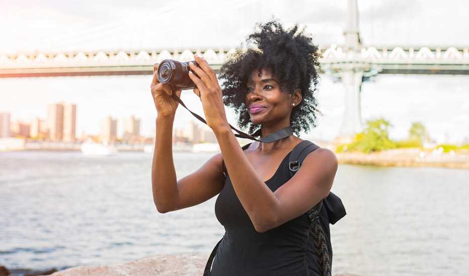 A woman taking a photo with a camera along a waterfront in a city