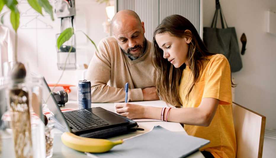 father helping his teenage daughter do homework with a laptop
