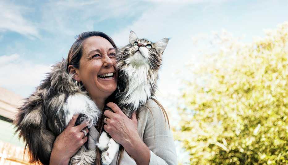 a woman holds her large fluffy cat on her shoulders