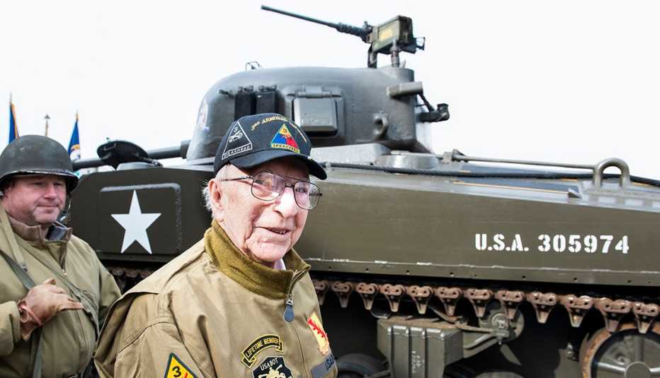 An older man stands next to a tank from World War Two