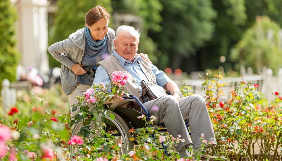 A woman pushes a man in a wheelchair through a row of flowers