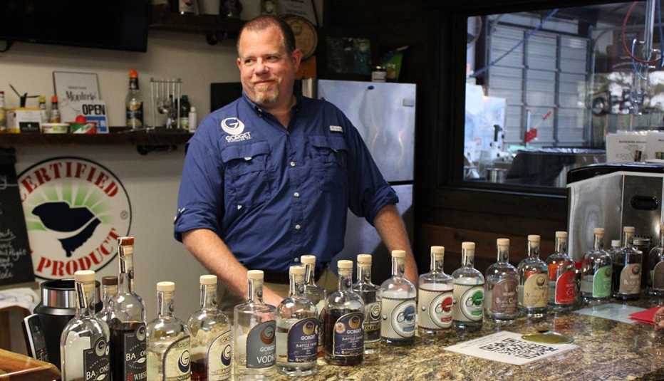 a man stands behind a bar with bottles of alcohol in front of him