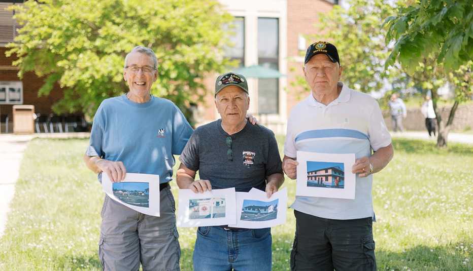 Three men hold photos of their time during the Vietnam War.