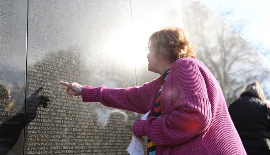 liz condon, dressed in a link sweater, uses her finger to scan names engraved into stone at the vietnam memorial