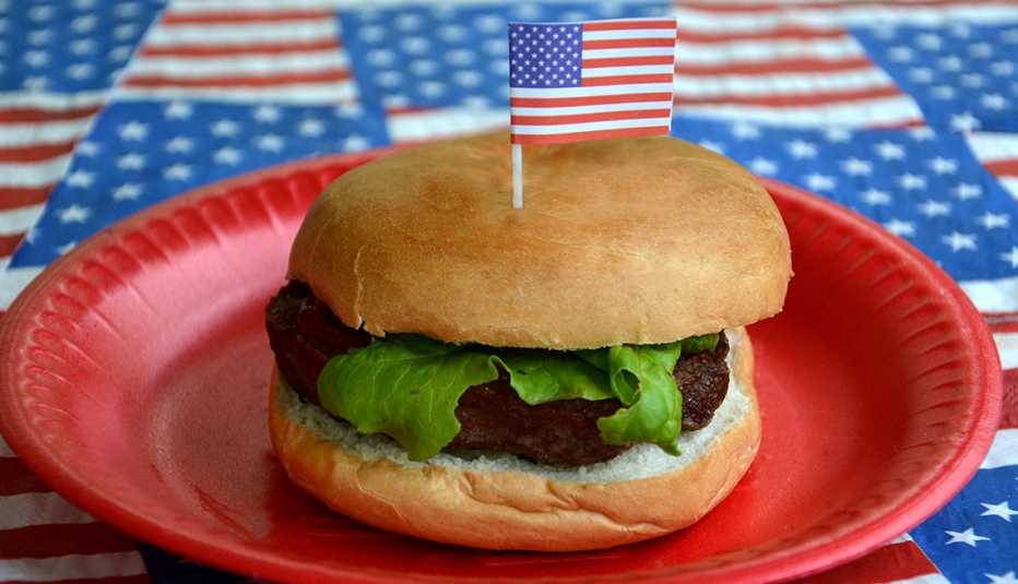 Single hamburger with lettuce Is topped with a small American flag. American flag tablecloth. 