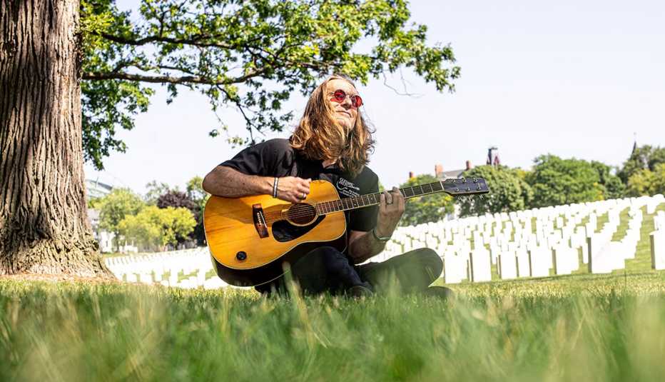 A person plays guitar in front of headstones