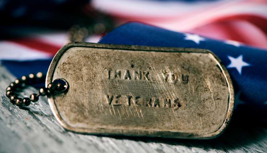 closeup of a rusty dog tag with the text thank you veterans engraved in it, next to a flag of the United States