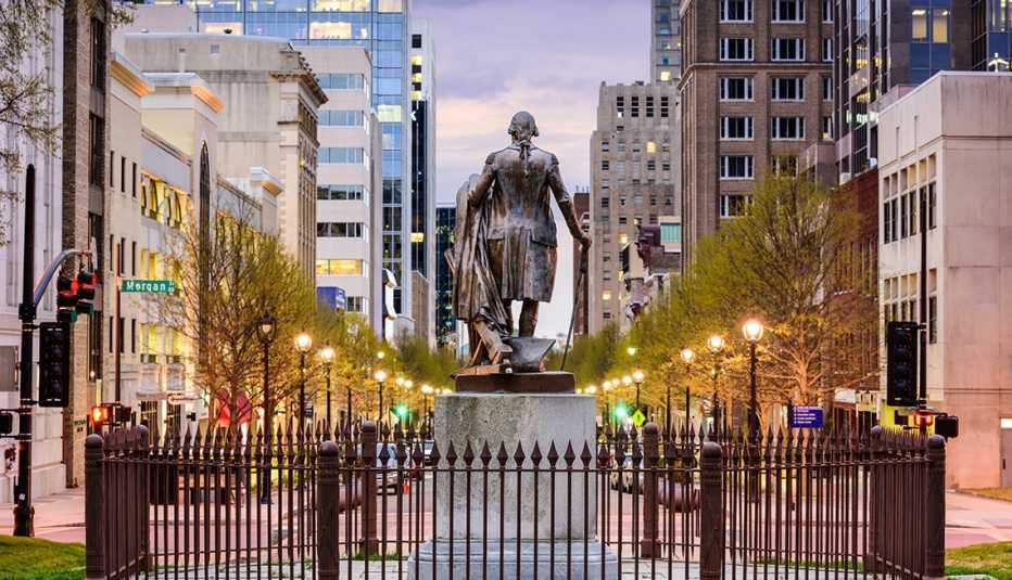 buildings line each side of the street. in the middle is an iron fence surrounding a statue of george washington in raleigh, north carolina.