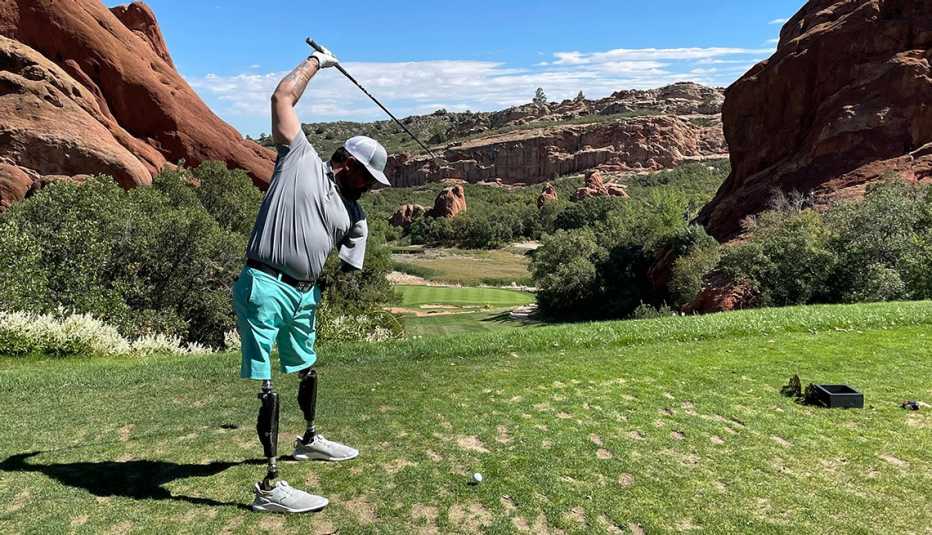 a man swings a golf club on a grassy course surrounded by rock formations