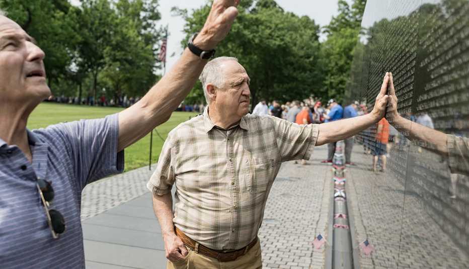 mike lowry and john lunsford visit the vietnam veterans memorial. one of the men places his hand on the wall, while the other gestures to a name above them.