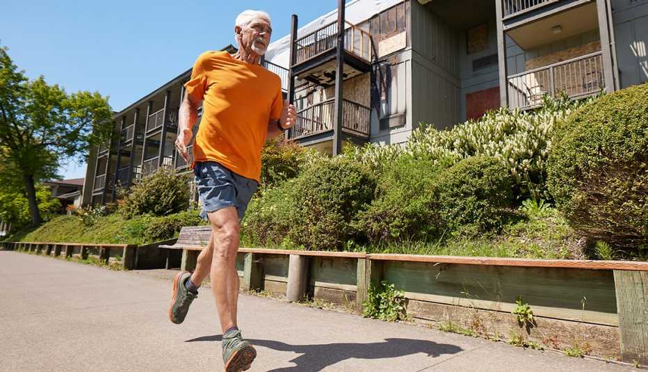a man, wearing gray shorts and an orange shirt, runs past an apartment complex.
