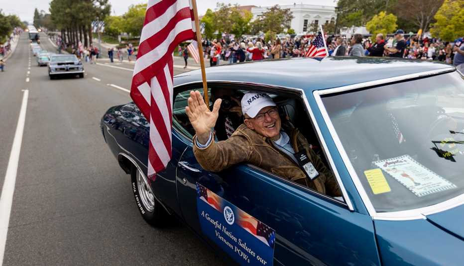 A man waves to crowds while riding in a classic car during a parade