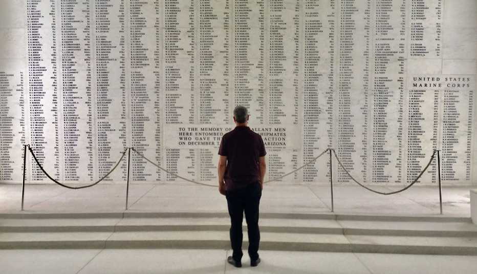 Gary Sinise stands in front of a wall with names of soldiers killed in the attack on Pearl Harbor.