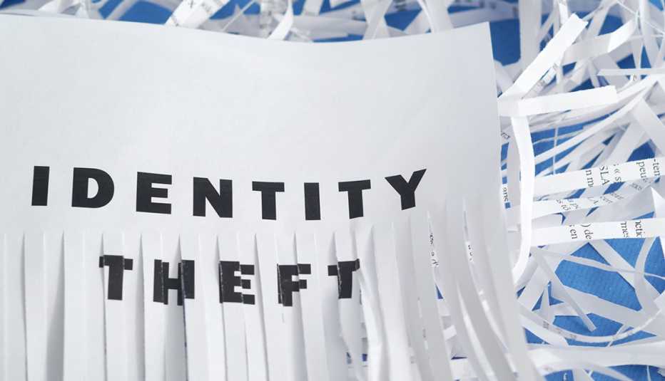 A sheet of paper with the words Identity Theft, lower half of the sheet is shredded with shredded paper in the background