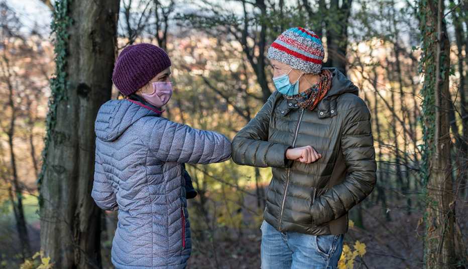 two women wearing protective face mask while hiking in the forest in cold weather.  Greeting with elbow