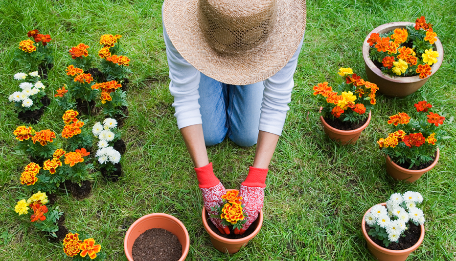 a person wearing a sun hat and long sleeves and gloves potting a flower
