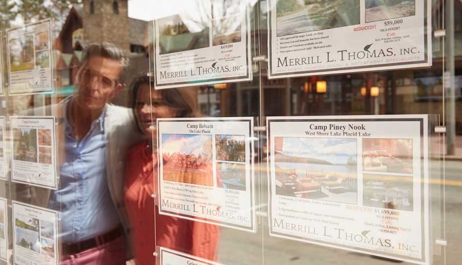 A man and woman looking at housing ads posted on a window. 