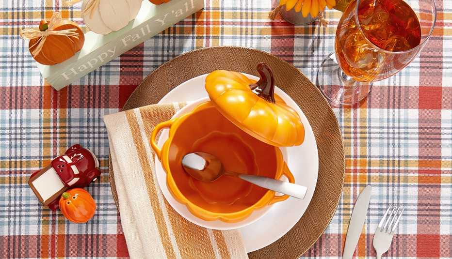 a fall table setting with a plaid tablecloth  a brown charger and white plate and a ceramic pumpkin shaped soup bowl