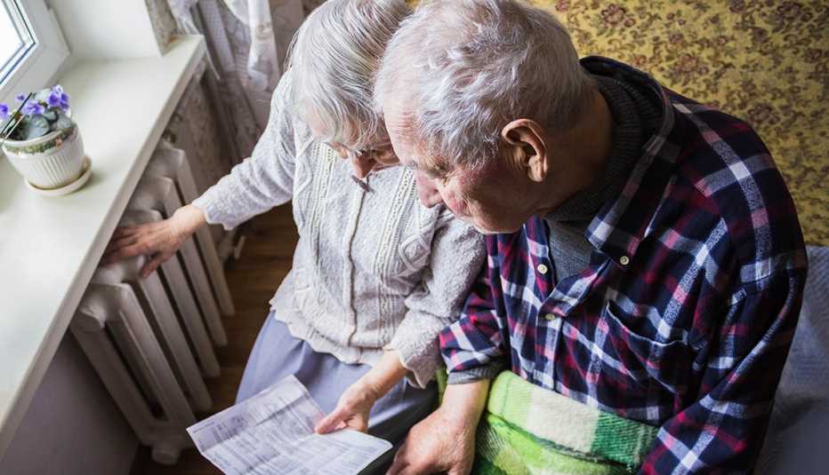 Senior couple hold gas bill and check radiator