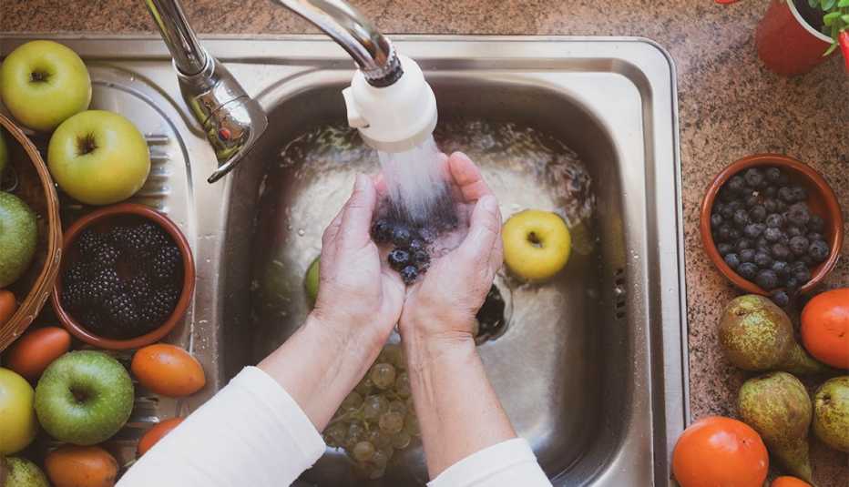 A woman's hands wash some fruit under the stream of water