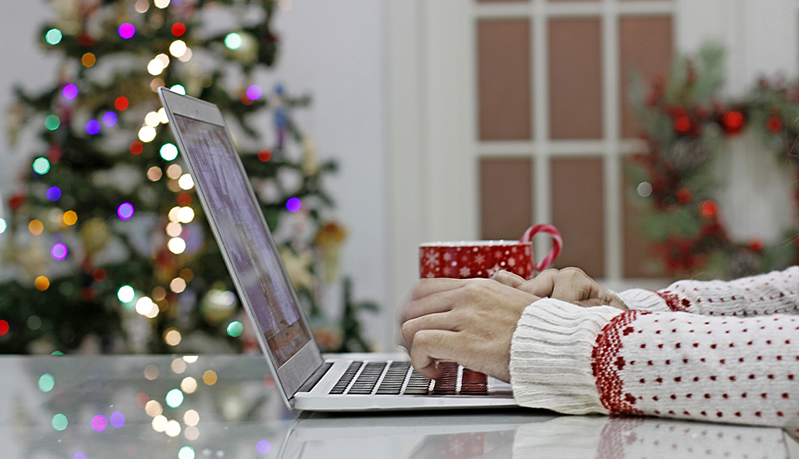 woman wearing a christmas sweater ordering gifts online at home from her laptop in front of the christmas tree