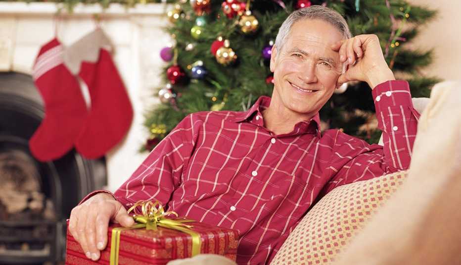 A smiling man sitting in living room holding a Christmas present