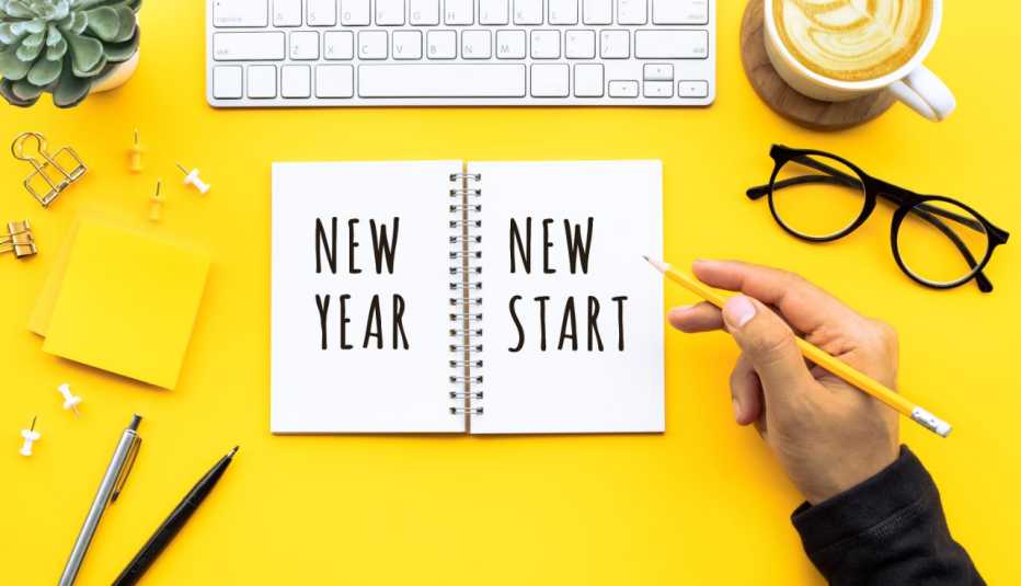 man writing new year fresh start in pencil on a white notebook on a bright yellow background