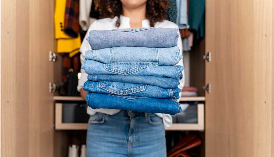 A woman standing in front of a wardrobe closet holding a stack of folded jeans
