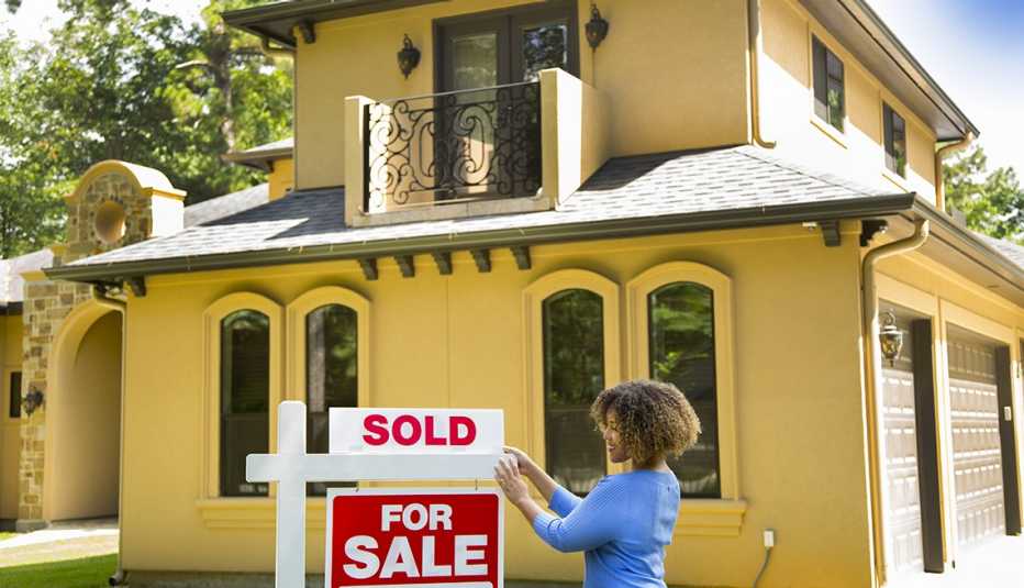 Realtor in front of a freshly painted yellow house adds a SOLD sign on top of a FOR SALE sign.