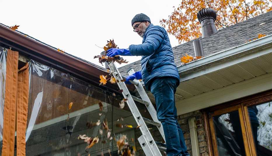 Man on ladder removing autumn leaves from gutter 