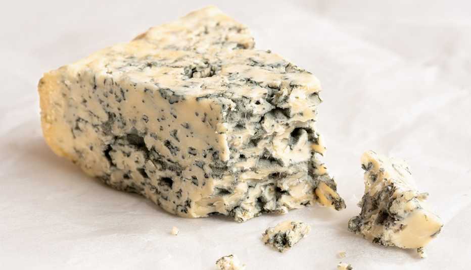 Broken blue cheese wedge with crumbles on wax paper
