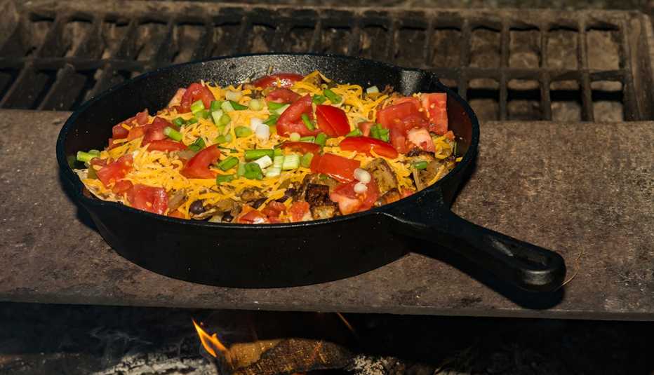 A cast iron skillet filled with nacho toppings placed over a campfire