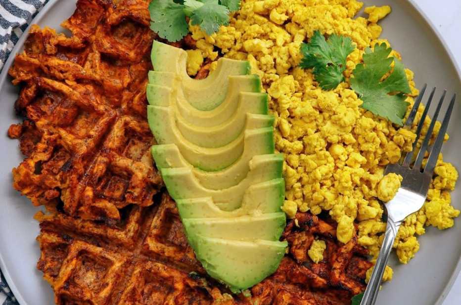 breakfast plate of a sweet potato waffle with scrambled eggs or tofu and sliced avocado