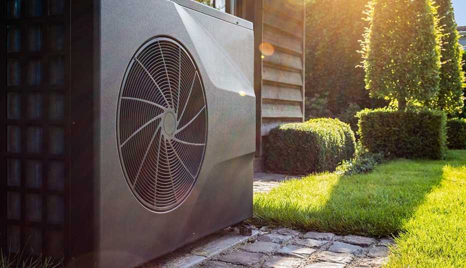 Close-up of black full inverter heat pump outside in the garden, near wooden pool house on a sunny day. 